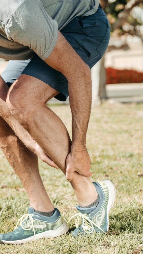 Adult male grabbing ankle due to injury in outdoor setting, wearing rubber running shoes.
